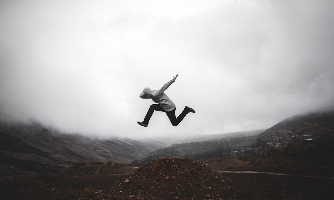 man in black jacket and pants jumping on brown rock formation during daytime
