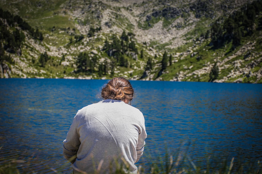 man in white long sleeve shirt sitting on green grass near body of water during daytime