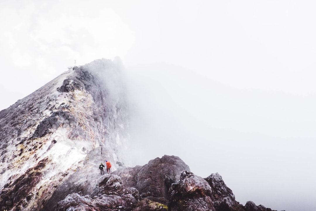 two people standing on mountain slightly covered with fogs during daytime