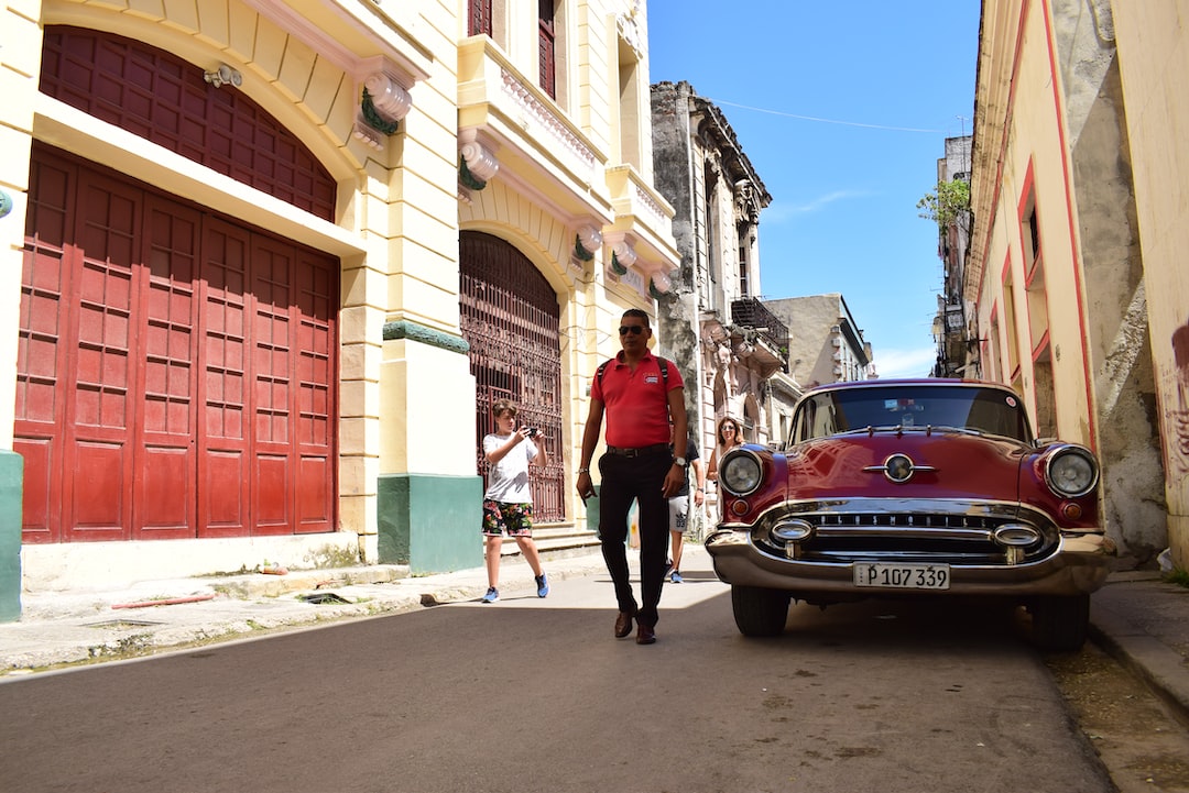 a man walking down a street next to a red car