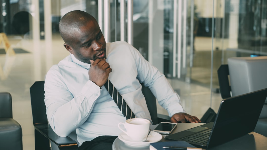 Man in shirt and tie working on laptop with coffee.